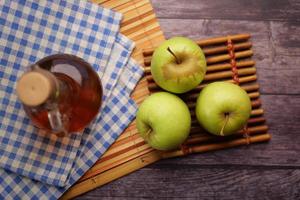 vinagre de maçã em frasco de vidro com maçã verde fresca na mesa foto