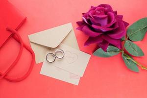 anel de casamento e caixa de presente e flor rosa em vermelho foto