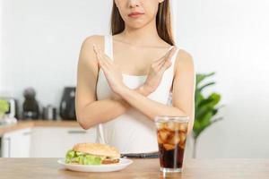 dieta, dieta mão do ásia jovem mulher negar, evitar Hamburger, lixo ou velozes Comida e espumante água, suave bebida, comer Comida para Boa saudável, saúde quando com fome. tentação do peso perda pessoas. foto