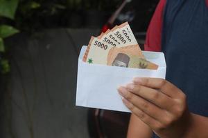 fechar acima do masculino mão inserindo cinco mil rupia dinheiro nota de banco para dentro envelope. financeiro e poupança conceito foto