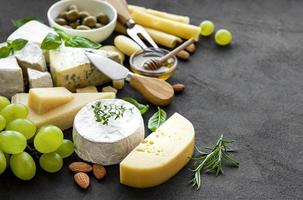 vários tipos de queijo, uvas, mel e salgadinhos em um fundo de concreto preto foto