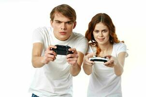 jovem casal dentro branco Camisetas com joysticks dentro seus mãos vídeo jogos entretenimento foto