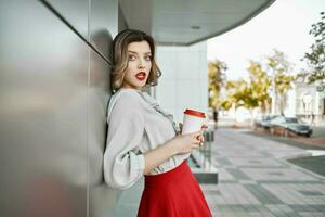 mulher dentro vermelho saia copo do café posando ao ar livre perto construção foto