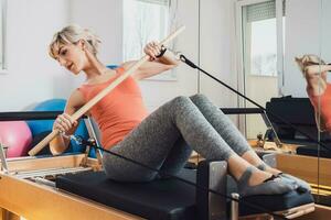 Loiras mulher é exercício em pilates reformador cama dentro dela lar. foto