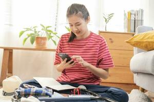 mochileiro viagem do feliz viagem ásia jovem mulher usando Móvel telefone levar Nota Verifica Lista embalagem ou preparar roupas para dentro bagagem, viagem caso para viagem viagem. viagem do viajante, feriado período de férias foto