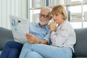 feliz marido e esposa Senior casal idosos família, caucasianos maduro, adulto amante e aposentado homem, mulher lendo jornal, relatório em sofá juntos às lar. marido e esposa estilo de vida. foto