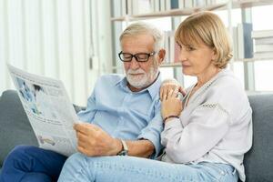 feliz marido e esposa Senior casal idosos família, caucasianos maduro, adulto amante e aposentado homem, mulher lendo jornal, relatório em sofá juntos às lar. marido e esposa estilo de vida. foto