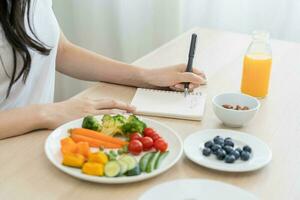 dieta, dieta mão do mulher escrever dieta plano certo nutrição em mesa com fresco legumes salada, amêndoa é diferente Comida ingredientes dentro a verde. nutricionista do saudável, nutrição do peso perda. foto