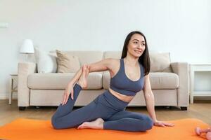 jovem atraente sorridente mulher praticando ioga, sentado dentro sereia pose, trabalhando fora, vestindo roupa de esporte, meditação sessão, interior cheio comprimento, casa interior foto