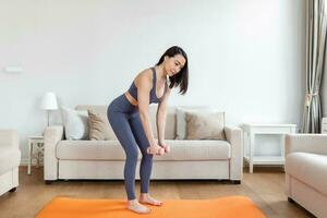 ásia mulher exercício com halteres às lar. feliz fêmea fazendo braço exercite-se usando halteres foto