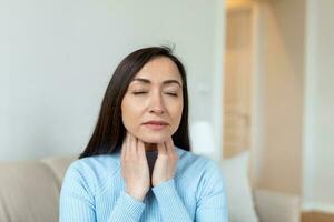 fechar acima do ásia mulher fricção dela inflamado amígdalas, amigdalite problema, cortado. mulher com tireoide glândula problema, tocante dela pescoço, mulher tem uma dolorido garganta foto