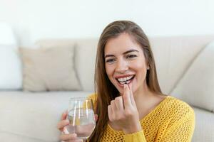 cabeça tiro sorridente jovem mulher segurando comprimido e vidro do fresco puro água. saudável milenar senhora levando antioxidante remédio vitaminas, beleza suplementos para cabelo pele unhas, cuidados de saúde conceito. foto