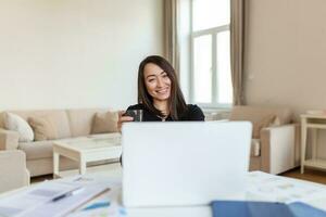 ásia mulher trabalhando em computador portátil computador, sorridente. mulher trabalhando a partir de casa em computador portátil dentro moderno apartamento. na moda mulher trabalhando em computador portátil a partir de casa foto