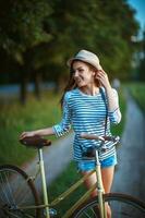 adorável jovem mulher dentro uma chapéu com uma bicicleta dentro uma parque foto