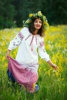 jovem sorridente menina dentro ucraniano traje com uma guirlanda em dele cabeça dentro uma Prado foto