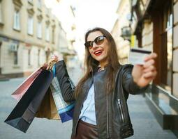 lindo mulher com compras bolsas e crédito cartão dentro a mãos em uma rua foto