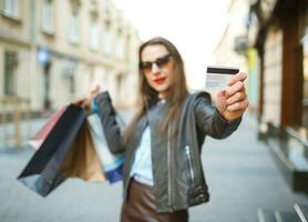 lindo mulher com compras bolsas e crédito cartão dentro a mãos em uma rua foto