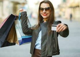 lindo mulher com compras bolsas e crédito cartão dentro a mãos em uma rua foto