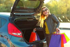 caucasiano mulher colocando dela compras bolsas para dentro a carro tronco foto