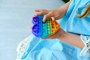criança jogando com arco Iris pop isto inquietação brinquedo. empurrar bolha inquietação sensorial brinquedo - lavável e reutilizável silício estresse alívio brinquedo. antiestresse brinquedo para criança com especial precisa. foto