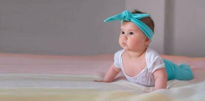 bandeira. bebê às 6 meses levanta dele corpo e aprende para arrastar. uma pequeno menina mentiras em dela estômago em a cama. uma lindo arco de cabelo para uma criança. foto