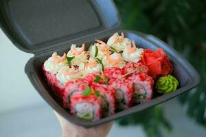 uma conjunto do Sushi e rolos dentro uma Preto caixa decorado com microgreens. Comida Entrega. Califórnia rolos com camarão. foto