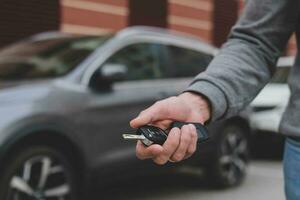 homem dentro frente do a Novo carro e segurando chaves. vendedor é carregando a carro chaves entregue para a cliente às a sala de exposições com uma baixo interesse oferecer. aluguel, crédito, seguro, carro comprar. cópia de espaço foto