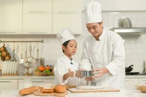 jovem ásia pai e dele filho vestindo chefe de cozinha uniforme cozimento juntos dentro cozinha às casa foto