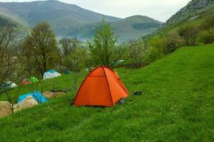 acampamento tendas em uma verde Prado dentro a montanhas dentro Primavera. descansar com a barraca dentro natureza foto