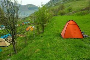 acampamento tendas em uma verde Prado dentro a montanhas dentro Primavera. descansar com a barraca dentro natureza foto