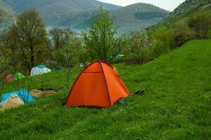 acampamento tendas em uma verde Prado dentro a montanhas dentro Primavera. descansar com a barraca dentro natureza foto