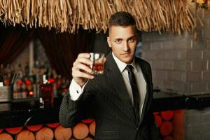 bonito jovem homem dentro uma à moda terno bebendo uísque dentro a bar. foto