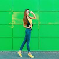 moda jovem lindo mulher dentro oculos de sol em pé perto a brilhante verde muro. foto