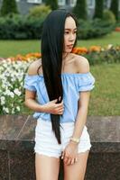 vietnamita lindo mulher com grandes cabelo dentro uma azul blusa posando dentro parque perto flores foto