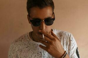 jovem hipster homem com oculos de sol e Penteado fumar uma cigarro. foto