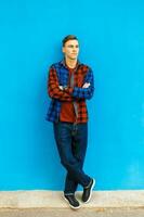 jovem bonito homem dentro à moda roupas e tênis poses perto a azul parede foto