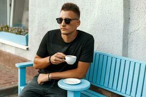 bonito jovem homem com café sentado em uma banco. foto