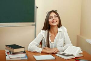 lindo jovem menina com uma sorriso, sentado em escola escrivaninha com livros. costas para escola foto