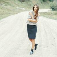 lindo menina modelo dentro uma cinzento suéter, saia e chuteiras caminhando em uma areia estrada. foto