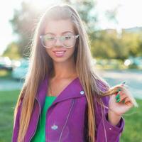 lindo alegre menina com uma doce sorrir dentro oculos de sol e uma brilhante colorida Jaqueta em uma ensolarado dia. foto