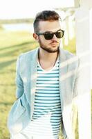bonito hipster homem dentro uma jaqueta, dentro uma verão camiseta e oculos de sol em uma ensolarado dia. foto