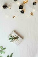 minimalista eco Natal. presente embrulhado dentro construir papel decorado com abeto galhos e uma festão em uma branco pano. topo e vertical Visão foto