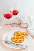 dois delicioso em forma de coração pizzas em pratos e dois óculos do vinho em uma conjunto mesa para comemoro dia dos namorados dia. vertical Visão foto