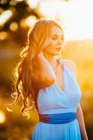 loira com cabelo solto em um vestido azul claro à luz do pôr do sol foto