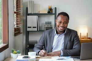 a africano americano homem de negocios dentro uma Preto terno sorridente e mostrando alegria às a da empresa anual lucro para Construir confiança para clientes quem vai investir dentro a escritório. foto