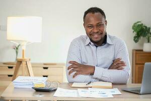 africano americano homem de negocios sorridente relaxado e cruzado braços depois de análise e pesquisa às casa escritório foto