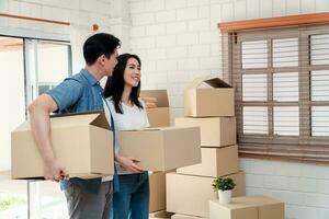 feliz jovem casal carregando cartão caixas e caminhando a partir de a frente porta para dentro a casa dentro uma Novo casa às comovente dia. conceito do realocação, aluguel, e proprietário comovente às lar. foto