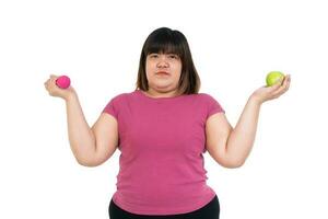 excesso de peso ásia mulher sentado e segurando uma verde maçã e halteres em isolado branco fundo. conceito do dieta, saúde Cuidado, e comendo Comida este é Boa para Boa saúde, e exercício, exercite-se foto