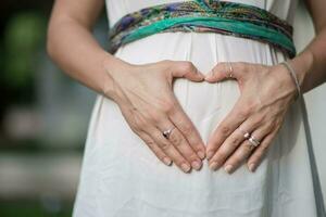 imagem do grávida mulher mãos Como uma coração forma em barriga foto