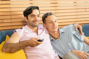 dois homens dentro casual roupas sentado em sofá abraçando e assistindo televisão com Cerveja e pizza dentro vivo quarto às lar. lgbt gay relação conceito. foto